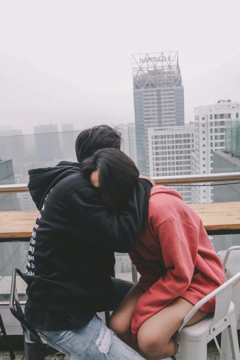 A young couple shares a warm embrace on a rooftop in Hanoi, Vietnam, with cityscape views.
